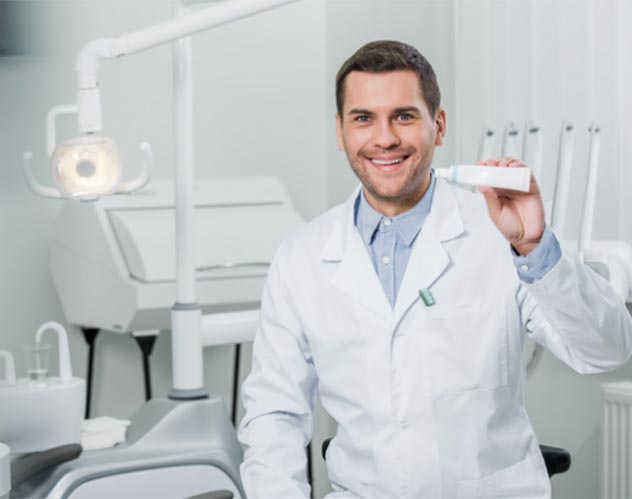 Ein Zahnarzt im Behandlungszimmer halt Zahnpasta hoch 