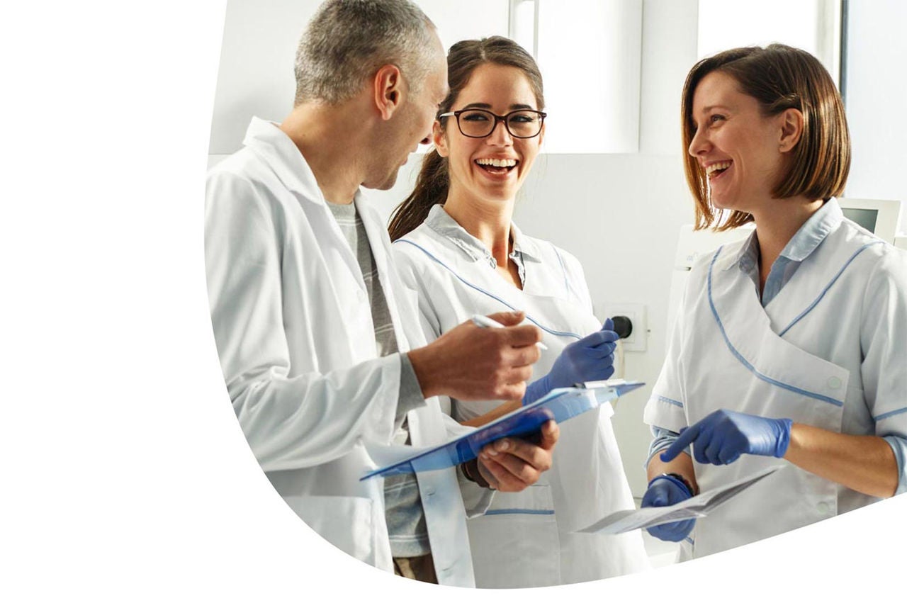 Drei lächelnde Zahnärzte stehen in einem Praxisraum